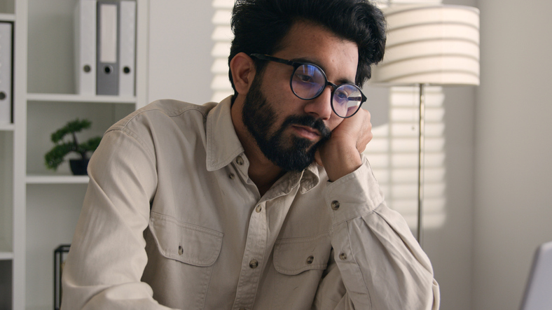 Tired exhausted weary Arabian Indian businessman bored employee designer sad sleepy unproductive at modern office work with laptop computer project boring burnout apathy business man lazy write notes