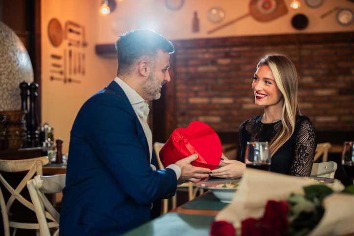 A couple enjoying a romantic dinner as the husband hands his wife a heart-shaped present
