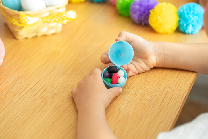 Child opening easter egg with colorful candy surrounded by festive decorations for spring celebration. Easter.