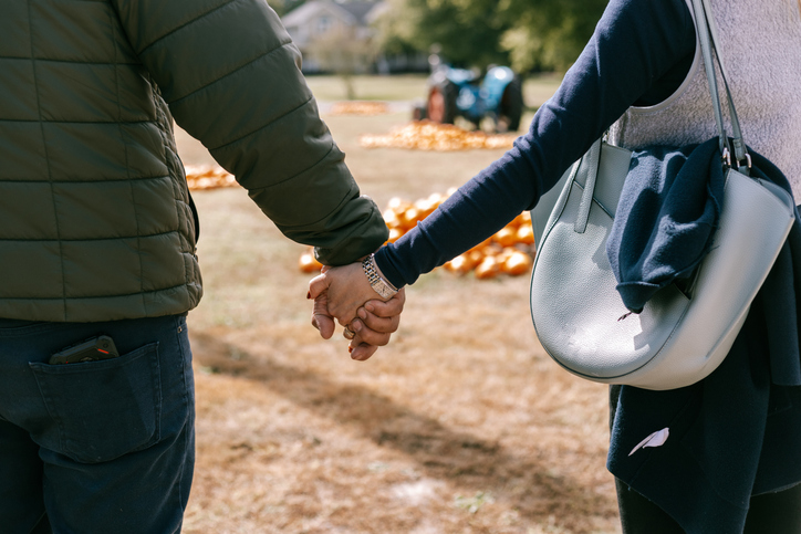 Couple holding hands at a pumpkin patch.