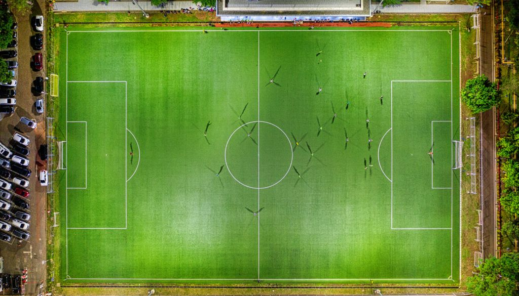 Aerial view of a soccer field with players on the pitch and surrounding buildings.