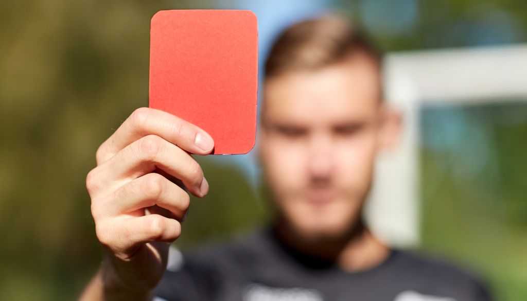 A person's hand holding up a red card, possibly a referee's card, with a blurred background.