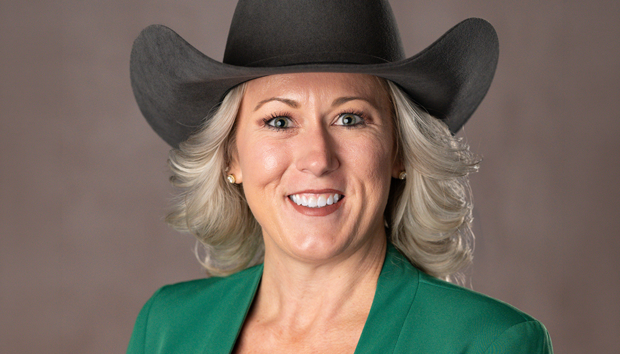 A smiling woman wearing a green jacket and a black cowboy hat.