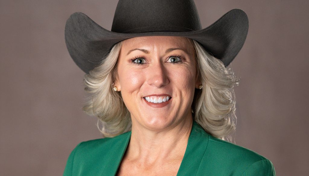 A smiling woman wearing a green jacket and a black cowboy hat.