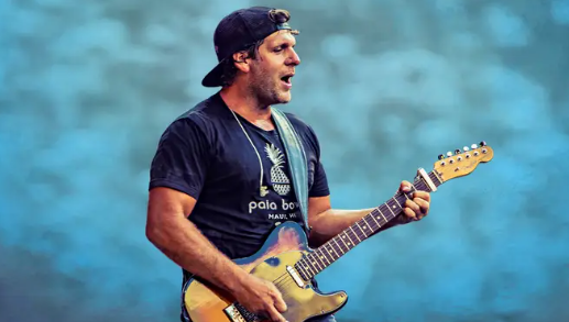 A man playing an electric guitar on stage, wearing a black t-shirt with "Polo Bear" logo.
