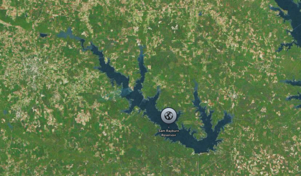 Aerial view of a large lake or reservoir surrounded by forested and rural areas, with the text "Sam Rayburn Reservoir" visible.