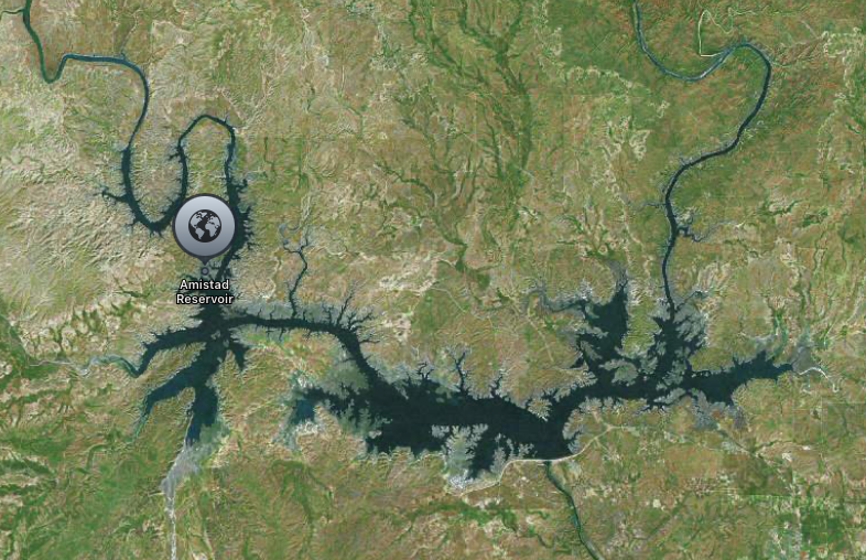 Aerial view of Amistad Reservoir surrounded by rugged, forested terrain.